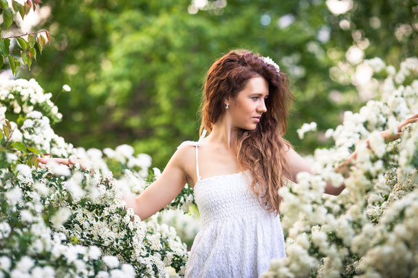 Charming young lady with beautiful smile in spring garden full of white flowers - Photo, Image