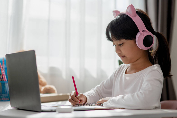 Asijské holčička ve sluchátkách mají video hovor vzdálené třídy s učitelem pomocí notebooku, studium on-line na počítači, domácí výuka koncepce - Fotografie, Obrázek