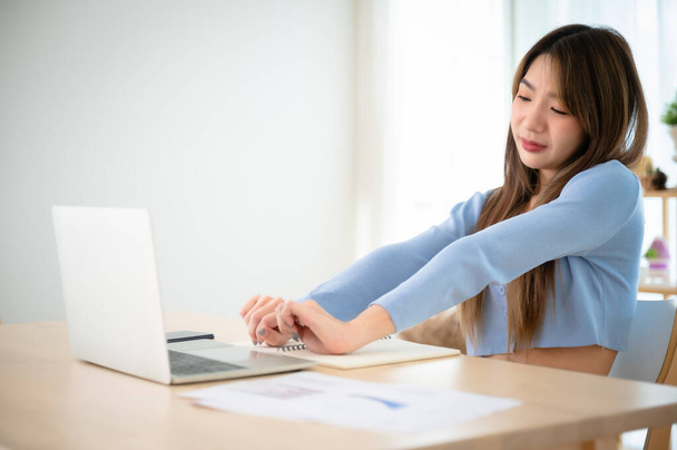 Irodai szindróma koncepció. Fiatal ázsiai nő fájdalmat érez a nyakában és a vállában, miután sokáig dolgozott a számítógép laptopján. Nyújtózik, hogy ellazítsa az izmait. - Fotó, kép
