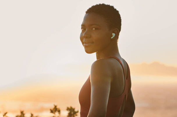 Portré, fekete nő és fitness edzés zenével, egészséges edzés vagy testmozgás naplementében. Afrikai sportlány, sportoló mosoly és kardio edzés, hallgatás vagy streaming motivációs podcast. - Fotó, kép