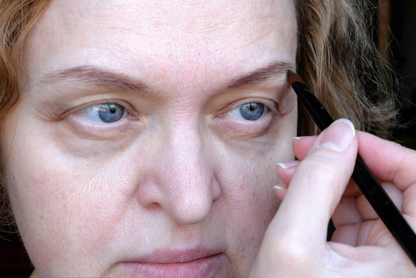 Keski-ikäisen naisen silmä roikkuvat silmäluomet tekevät kulmakarvojen meikkiä. Ptoosi on ylemmän silmäluomen roikkuminen, laiska silmä. Kosmetologia ja kasvojen käsite, ensimmäinen ryppyjä, lähikuva - Valokuva, kuva