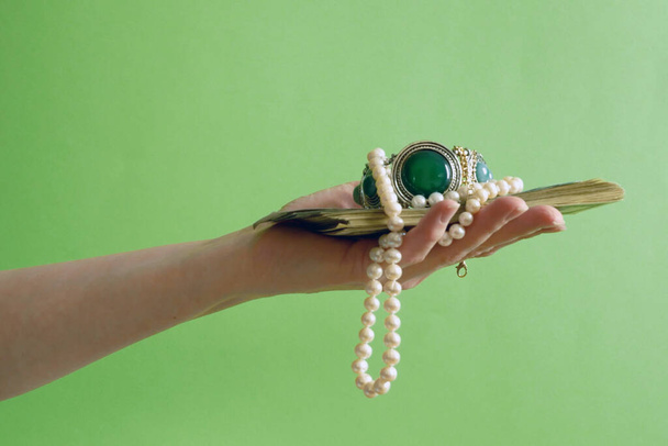 緑の石、真珠のネックレスと黄金の宝石緑の背景とヴィンテージ銀のブレスレットを保持手、クローズアップ - 写真・画像