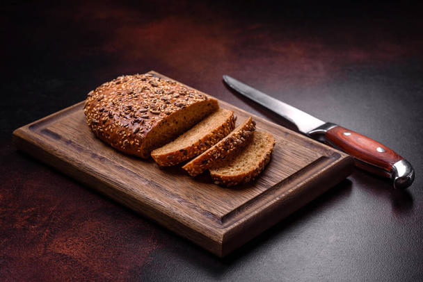 Pyszny chrupiący chleb ze zbożem na drewnianej desce do krojenia na ciemnym betonowym tle - Zdjęcie, obraz