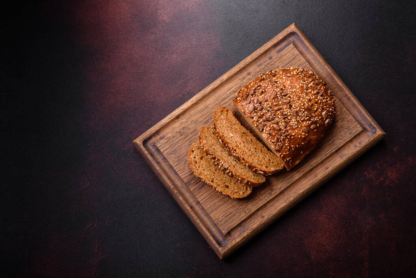 Νόστιμο τραγανό ψωμί με δημητριακά σε ξύλινο ξύλο κοπής σε σκούρο μπετόν φόντο - Φωτογραφία, εικόνα