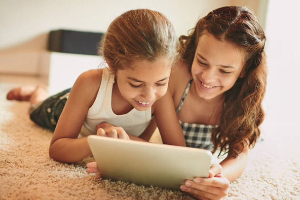 Deze app is zo cool. twee jonge meisjes met behulp van een digitale tablet thuis - Foto, afbeelding