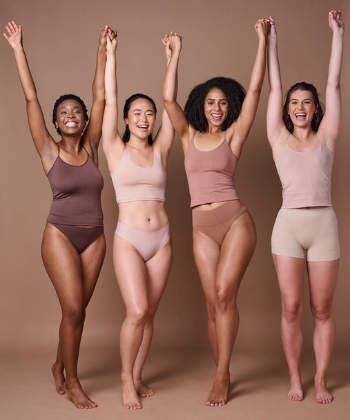 Diversiteit, vrouwen en natuurlijke schoonheidsvrienden in studio in bruine achtergrond met handen opgetrokken in viering en steun samen. Diverse vrouwen, ondergoed en vieren lichaamsverzorging of een gezonde levensstijl. - Foto, afbeelding