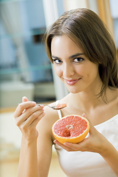 Portarit of young woman eating grapefruit at home - Fotó, kép