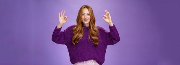 Bien, estoy de acuerdo. Retrato de amigable y optimista joven veinteañera jengibre en suéter púrpura levantando las manos con el gesto bien o bien sonriendo en aprobación, gustando producto fresco, dando recomendación. - Foto, imagen