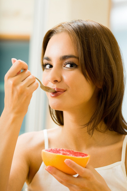 Young woman eating grapefruit at home - Φωτογραφία, εικόνα