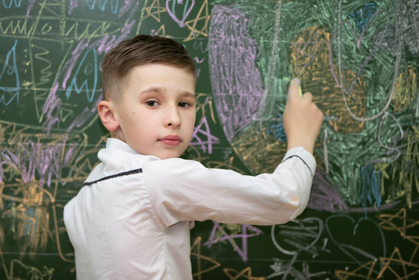 The schoolboy at the blackboard draws with chalk. Middle school age. The boy is in the classroom. - Photo, Image