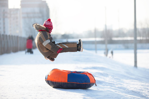 A happy boy up in the air on a tube sledding in the snow.. A boy slides down a hill in winter. - Foto, Imagen