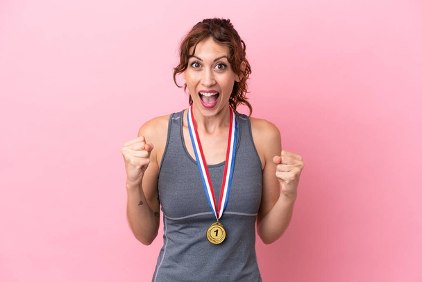 Joven mujer caucásica con medallas aisladas sobre fondo rosa celebrando una victoria en posición ganadora - Foto, imagen