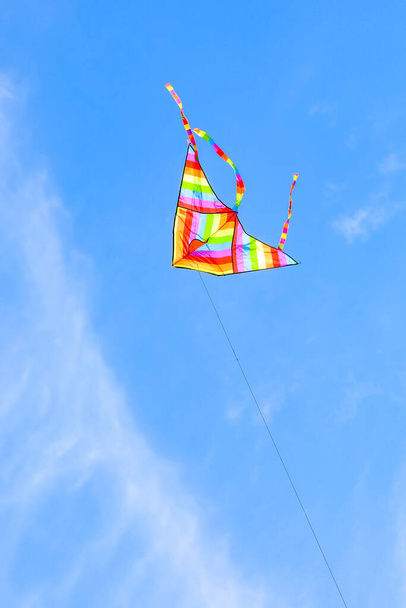 grote regenboog gekleurde vlieger vliegen hoog in de blauwe lucht met een aantal witte wolken - Foto, afbeelding