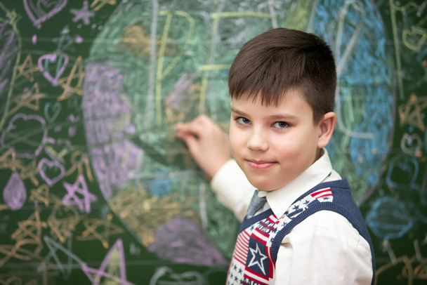 The schoolboy at the blackboard draws with chalk. Middle school age. The boy is in the classroom. - Photo, Image