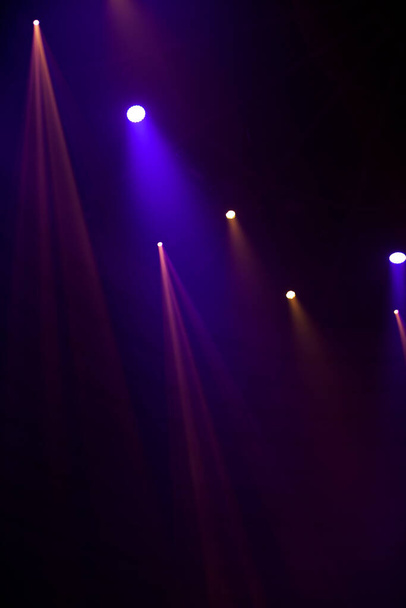 Paarse lichtstralen van podiumspots op een donkere achtergrond. - Foto, afbeelding