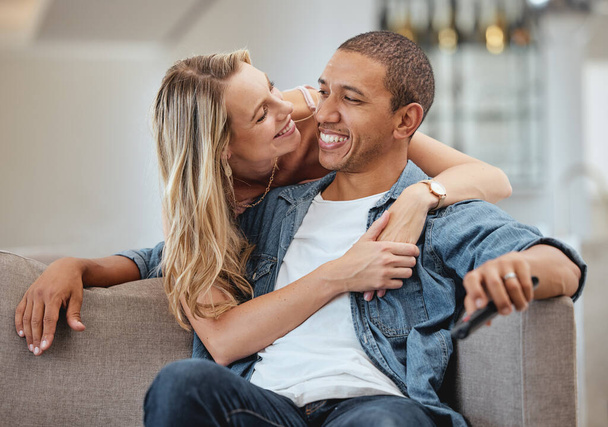 Szerelem, boldogság és mosoly egy sokszínű párral, akik egy kanapén ölelkeznek az otthonuk nappalijában. Támogatás, romantika és ragaszkodás egy férfi és nő megosztani egy intim pillanat egy házban. - Fotó, kép