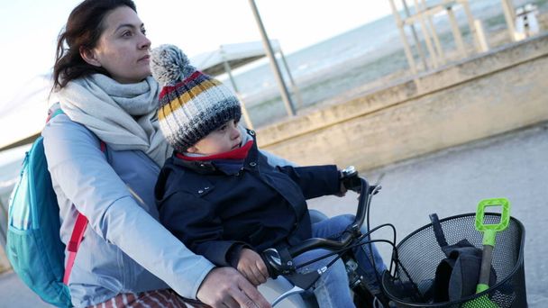 Mutter und 2-jähriges Kind während des kalten Wintertages draußen auf dem Fahrrad. Kind und Eltern mit Schal und Jacke fahren Fahrrad - Foto, Bild