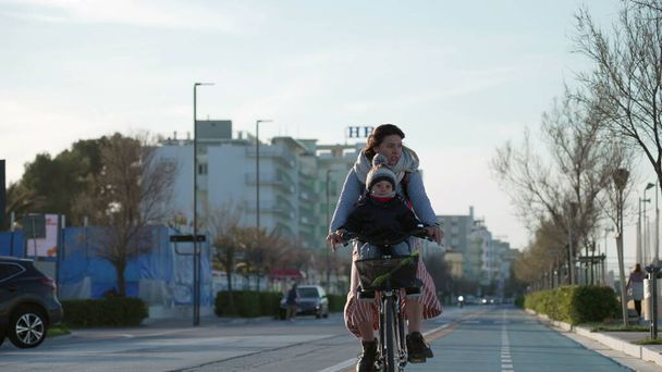 Mãe anda de bicicleta com criança na frente em ciclovia pela costa do mar. Bicicleta de equitação parental ao ar livre durante o dia frio - Foto, Imagem