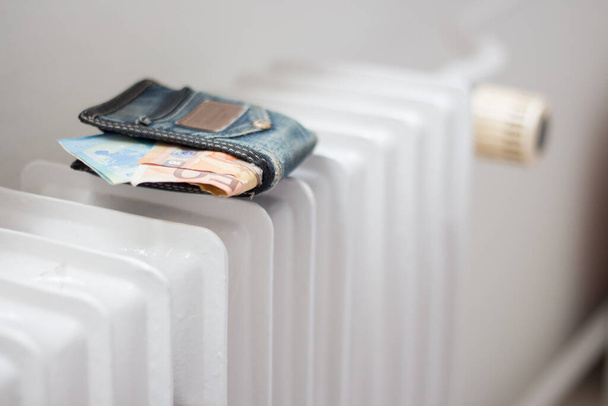 Wallet with money on the heating radiator in the apartment. Increasing the cost of energy due to the war in Ukraine - Photo, Image