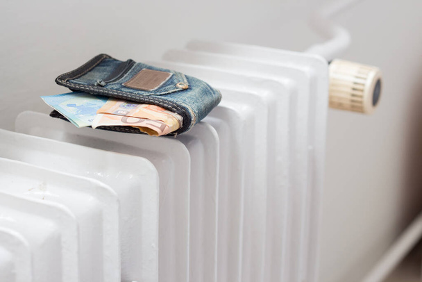 Бумажник с деньгами на обогревателе в квартире. Увеличение стоимости энергии в связи с войной на Украине - Фото, изображение