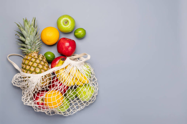 Shopping mesh bag vol met gezond fruit voedsel op grijze achtergrond. Vlakke lay met kopieerruimte - Foto, afbeelding