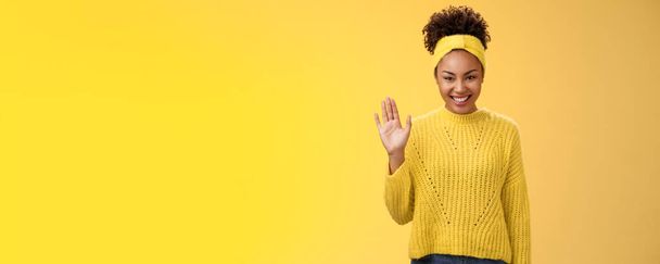 Cute timid friendly young girl wanna find new friends look pleasant smiling charmingly gladly waving hand hello hi gesture say welcome greeting heartwarming introduction herself, yellow background. - Photo, Image