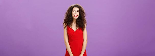 Studioaufnahme einer süßen, nachdenklichen und kreativen, charmanten Europäerin in stylischem roten Lippenlecken mit Lust und Belustigung, die in die rechte obere Ecke lächelt und mit Fantasie tagträumt. Kopie - Foto, Bild