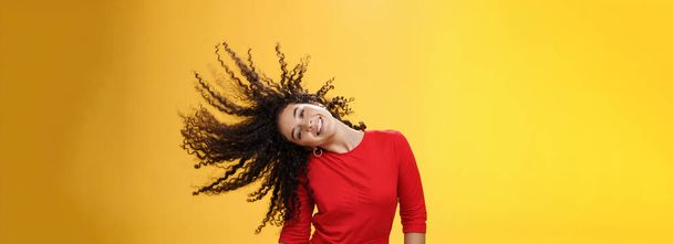 Girl getting carefree and wild waving hair and making sun with curls flying in air smiling broadly tilting head and having fun, dancing delighted and amused feeling playful against yellow background. - Photo, Image