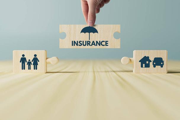 The hand holds a wooden block with an umbrella putting it on top of other blocks with icons of family, home, car, life. The concept of getting insured, insurance as an important element of life. - Photo, Image
