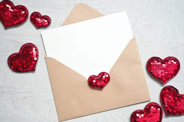 Tarjeta de felicitación blanca en blanco con sobre marrón y corazones sobre mesa de mármol. Concepto de día de San Valentín de burla - Foto, imagen