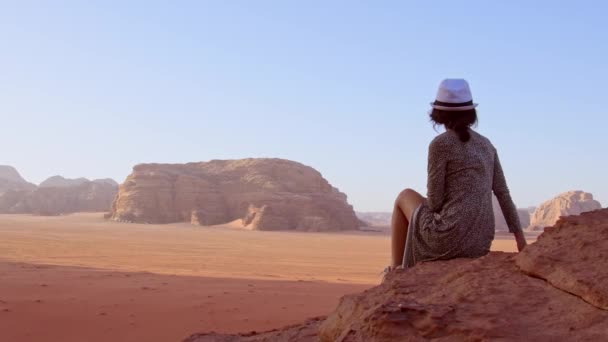 Donna turista in abito sedersi sulla scogliera al punto di vista sul tramonto nel deserto Wadi Rum valle Wadi Saabit. Giordania esplorare concetto - Filmati, video