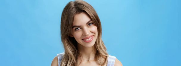 Περιμένετε-up πλάνο της γοητευτικής αυτοπεποίθηση αυθεντική γυναίκα αισθάνεται μεγάλη αποδοχή δική ατέλειες γέρνοντας το κεφάλι χαμογελώντας ευρέως στην κάμερα και δείχνει χαριτωμένο σπασμένα δόντια ποζάρουν πάνω από το μπλε φόντο - Φωτογραφία, εικόνα