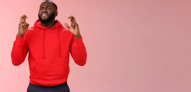Passionate devoted african-american male fan praying cross fingers good luck asking god win bet biting lip impatiently waiting important results supplicating hopefully, standing pink background. - Photo, Image