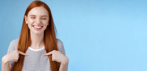 Happy cheerful glad young sportswoman redhead nominated smiling surprised laughing joyfully close eyes pointing herself chosen picked winning first prize, standing blue background. - Photo, Image