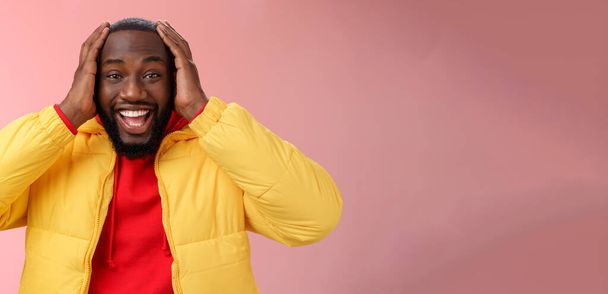 Счастлив удивлен порадовал молодой афроамериканец 25-летний мужчина молодой пиджак красный толстовка улыбаясь весело, удивлен улыбаясь получая удивительный подарок держа за руки взволнованной головой, стоя розовый фон. - Фото, изображение