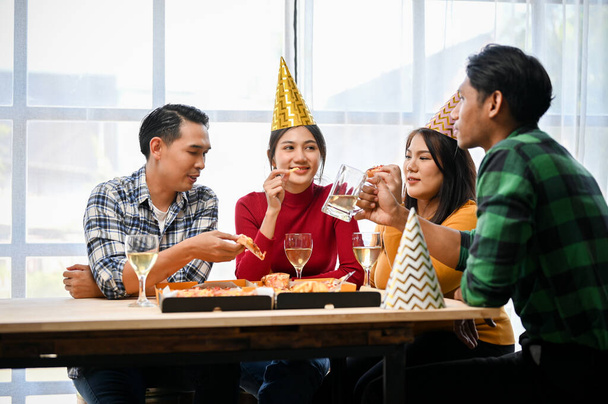 Ομάδα χαρούμενων και χαρούμενων Ασιατών φίλων απολαμβάνουν να μιλάνε πίνοντας μπύρα και τρώγοντας πίτσα μαζί στο πάρτι. - Φωτογραφία, εικόνα