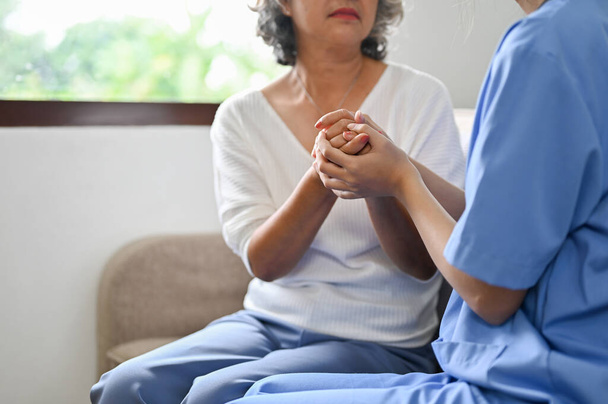 Eine Ärztin hält einer alten Patientin die Hand und gibt ihr während des Treffens Halt und Trost. zugeschnittenes und Nahaufnahme-Bild - Foto, Bild