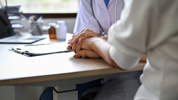 immagine ravvicinata, una dottoressa che tiene le mani della paziente sul tavolo mentre discute il piano di trattamento. - Foto, immagini