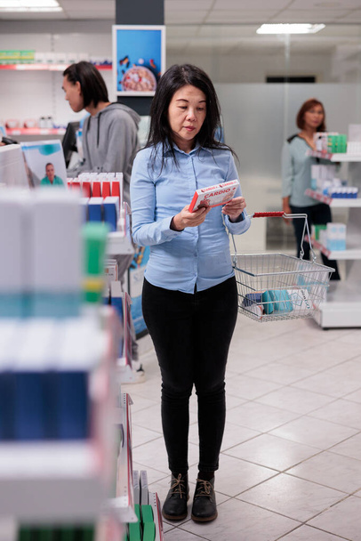 Азійські клієнти, які читають листівку з таблетками для таблеток, перш ніж купувати продукти охорони здоров'я в аптеках. Клієнт фармації дивиться на ліки та вітаміни, кардіологічні препарати.. - Фото, зображення