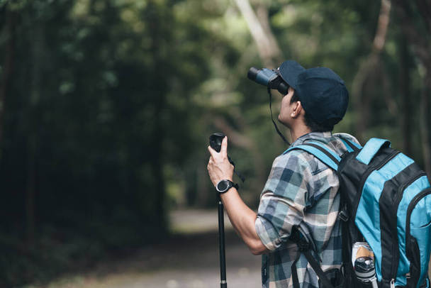 Hikers use binocular to see animals and view landscape  with backpacks walking through on the road in the forest. hiking and adventure concept. - Photo, Image