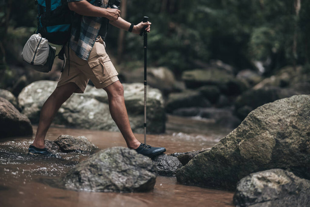 Hikers use trekking pole with backpacks walking through the rock and water on stream in the forest. hiking and adventure concept. - Fotografie, Obrázek