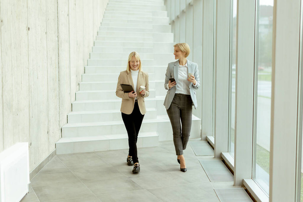 Dos mujeres de negocios caminando con tableta digital y teléfono móvil en el pasillo de la oficina - Foto, Imagen