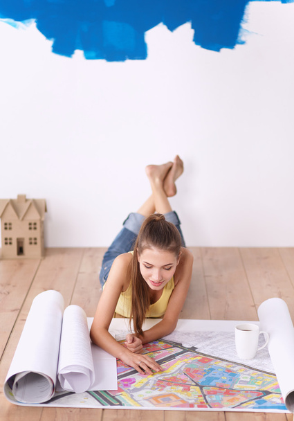 Young woman lying on the floor and looking at blueprint of new house - Фото, зображення
