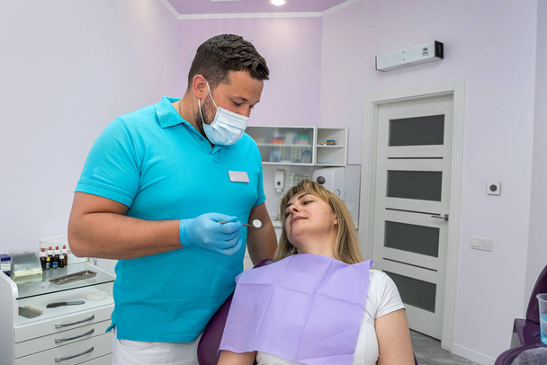 handsome male dentist in a mask examines the teeth of a patient. Dentist male examination concept - Zdjęcie, obraz