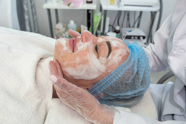 kozmetológus ecsettel alkalmazza a kozmetikai maszkot az arc egy ügyfél egy szépségszalonban. kozmetikai eljárások. szépségszalon - Fotó, kép
