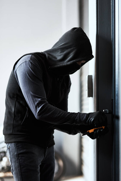 Hace que parezca tan fácil. un criminal enmascarado ocupado abriendo la cerradura de una puerta en un garaje - Foto, imagen