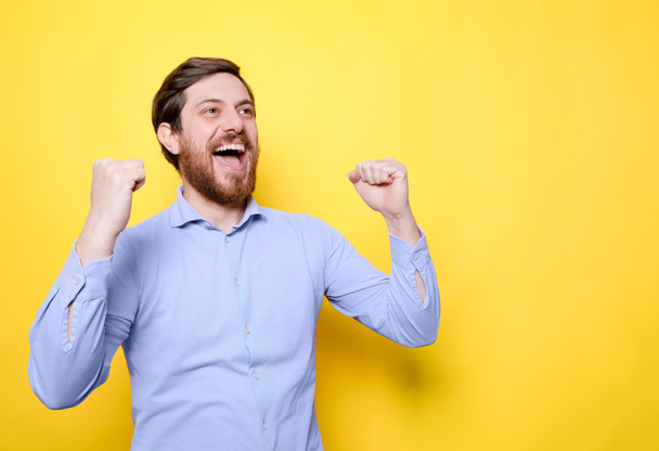 Glücklicher Mann feiert Erfolg mit geballten Fäusten auf gelbem Hintergrund - Foto, Bild