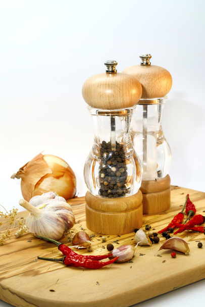 Соль и перец мельницы с ингредиентами вокруг на деревянной доске резки
 - Фото, изображение