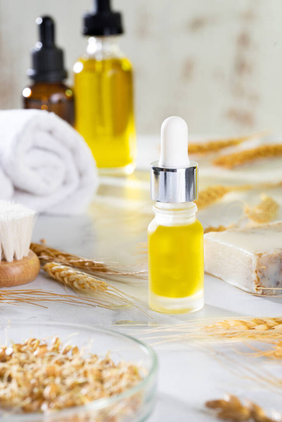 Oils, bath brush, towel and wheat sprouts on the cosmetic table in the bathroom. A set of organic cosmetics in glass vials with dropper for skin and hair care. The concept of self care and spa. - Photo, Image