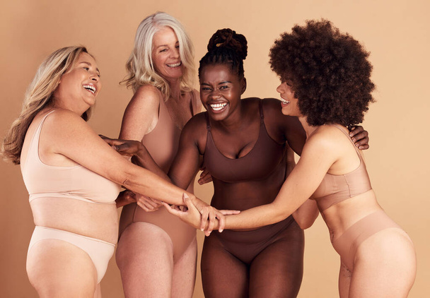 Krása, rozmanitost a skupina žen ve spodním prádle ve studiu izolovaných na hnědém pozadí. Spodní prádlo, přátelé a tělo pozitivní feny, sebelásku a držení za ruce pro posílení postavení, smích nebo úsměv. - Fotografie, Obrázek